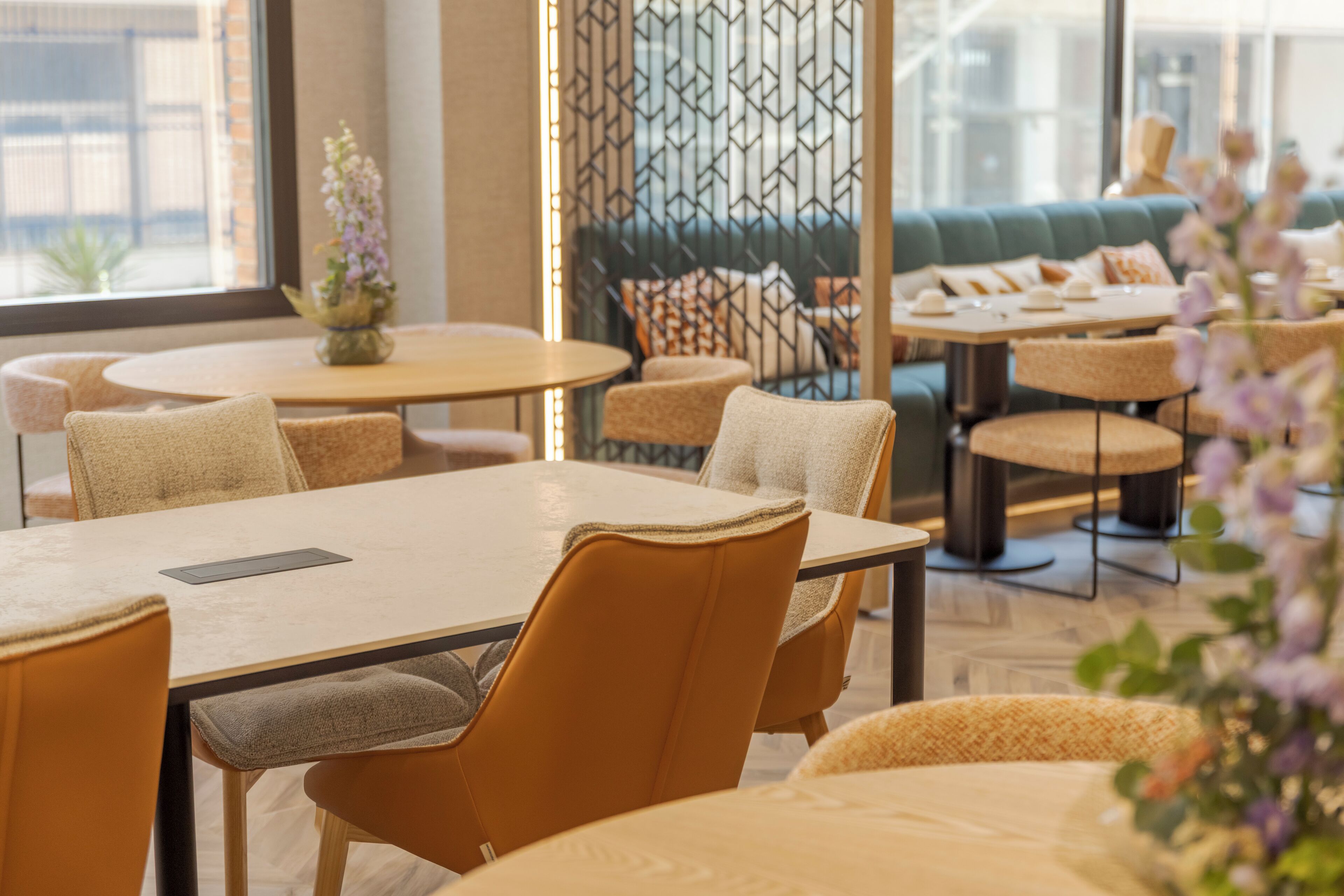 Un comedor moderno con mesas redondas y sillas acolchadas, un separador decorativo y vistas de la ciudad a través de amplios ventanales.