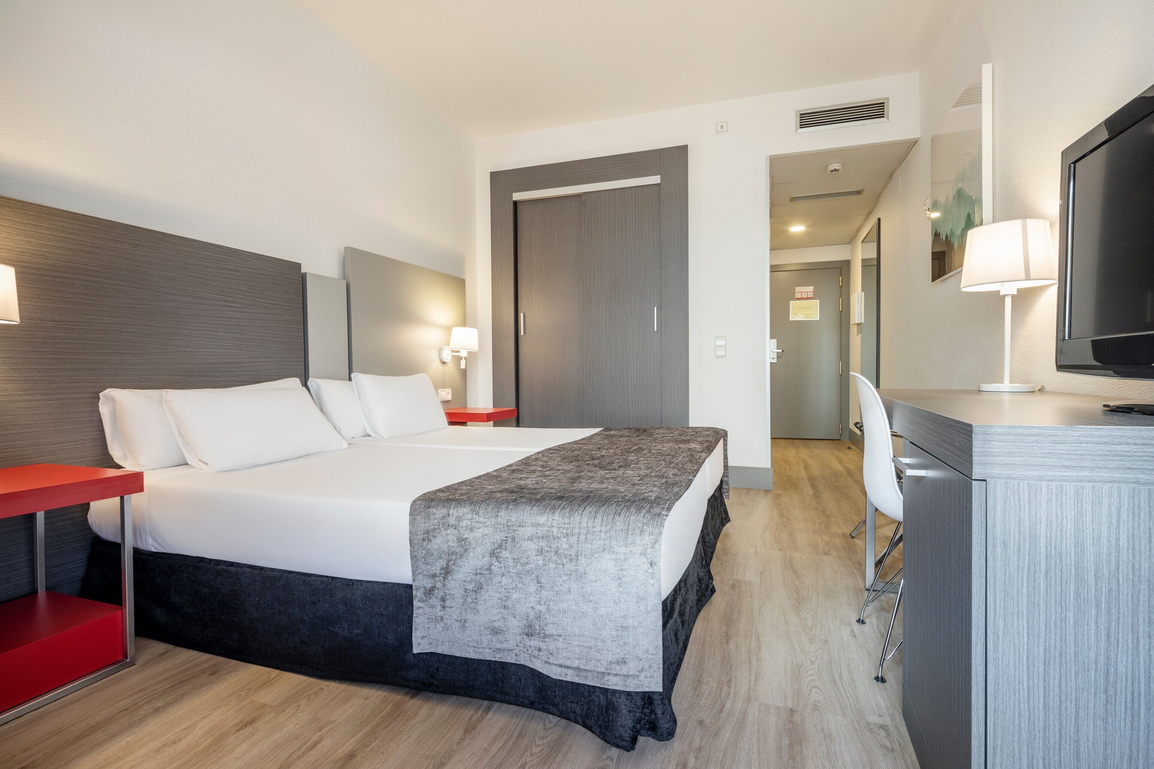 Quarto de hotel moderno com uma cama grande, mesas de cabeceira, uma escrivaninha e uma televisão.