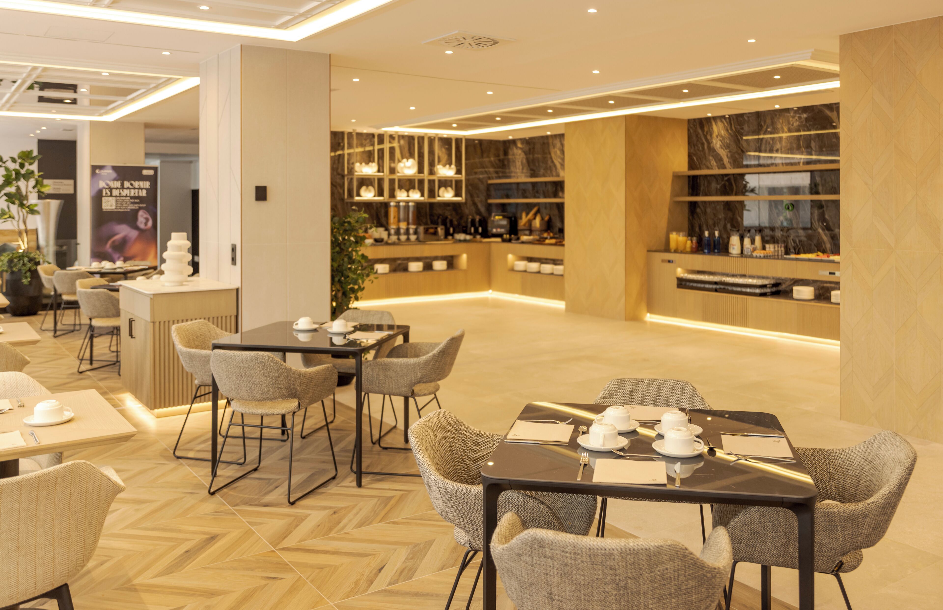 Un moderno vestíbulo de hotel con un área de estar central, una recepción y una zona de bar con estantes llenos de botellas y vasos.