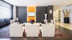 A modern hotel lobby with a seating area, a large vase, and a sign indicating the restaurant and assembly hall. - Hotel ILUNION Romareda (Zaragoza)