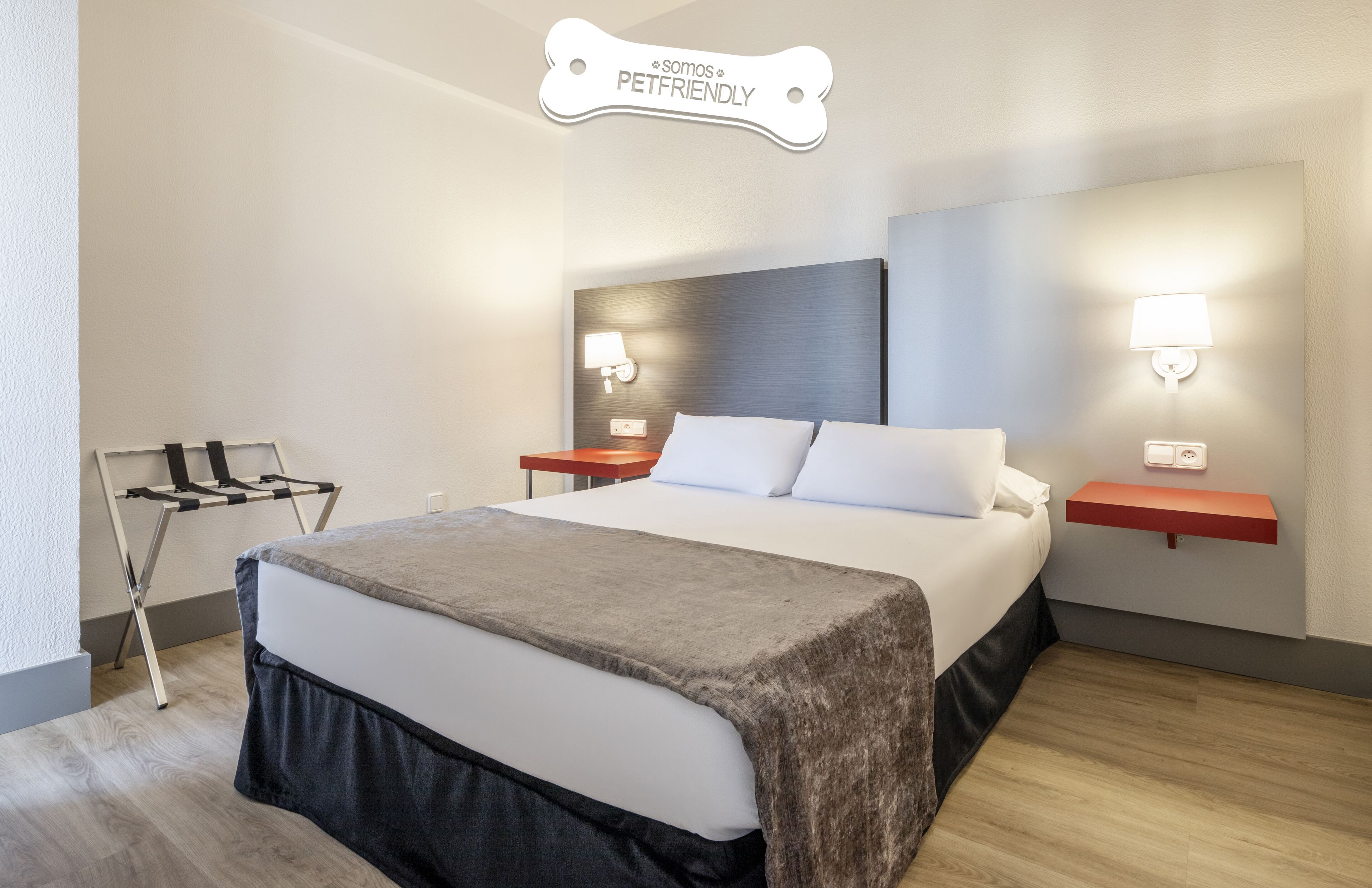 A hotel room with a large bed, a nightstand, a wall-mounted lamp, a pet-friendly sign, and a coat rack.