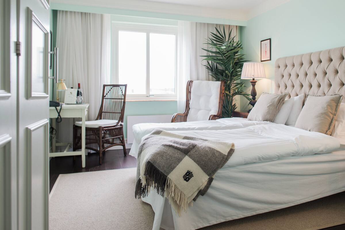 A hotel room with a bed, a chair, a desk, a lamp, and a plant.