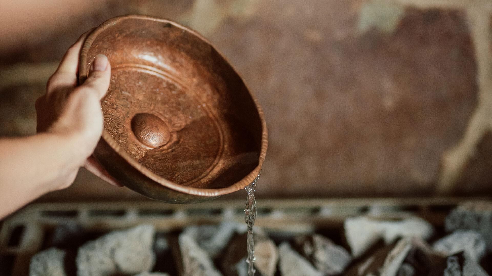 Eine Hand hält eine Holzkreislaufschale, aus der Wasser fließt.