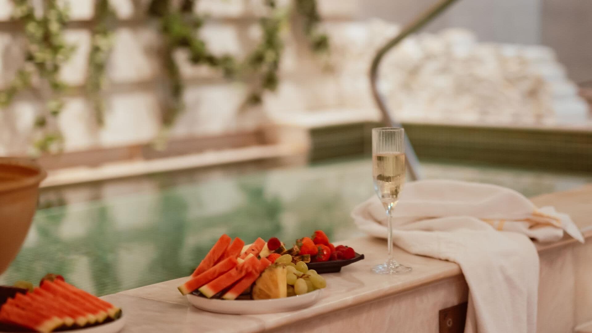 A poolside setting with a fruit platter and a glass of champagne on a table.