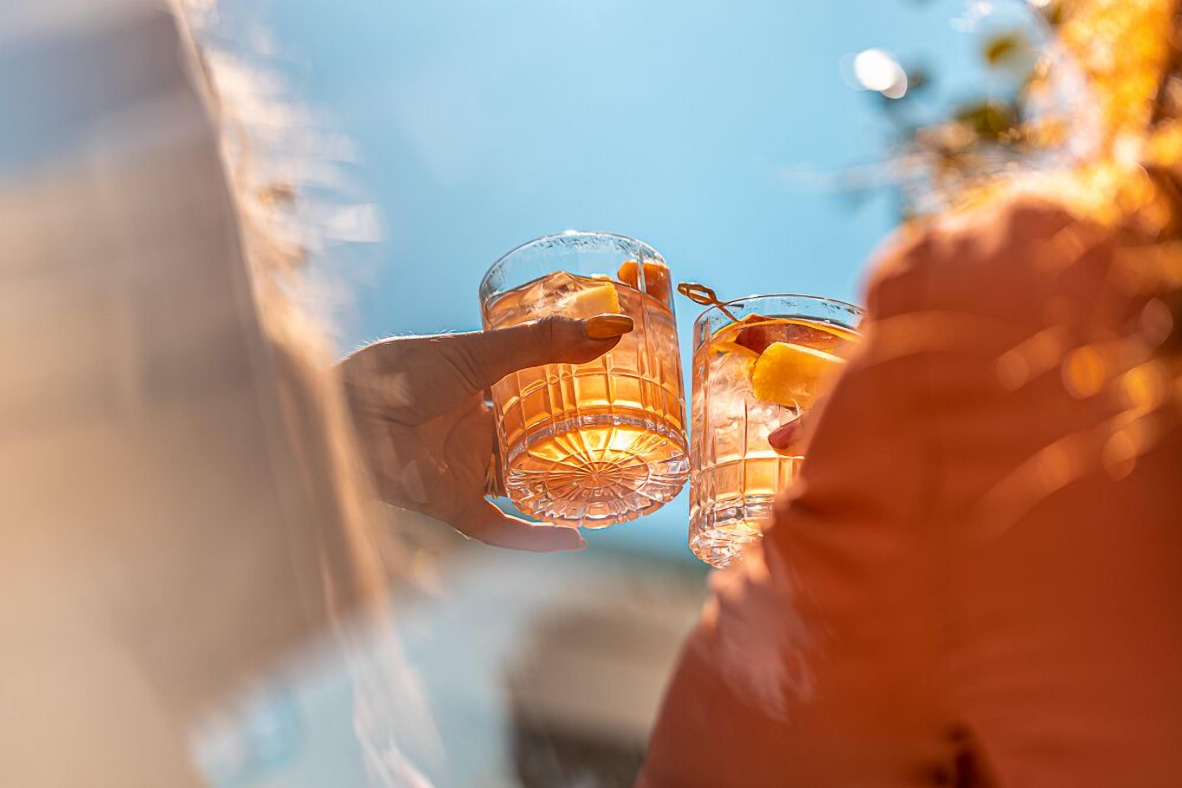 Two clear glasses with ice cubes and a lemon slice, held by a person.