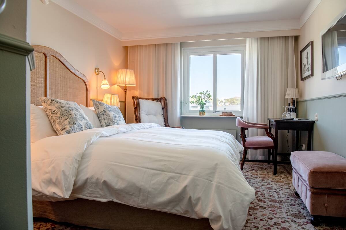 A hotel room with a large bed, a desk, a chair, and a window with curtains.