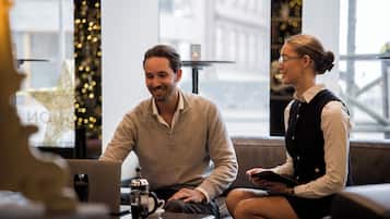 Un interior moderno con una laptop sobre una mesa, una cafetera y una persona sentada en un sofá.