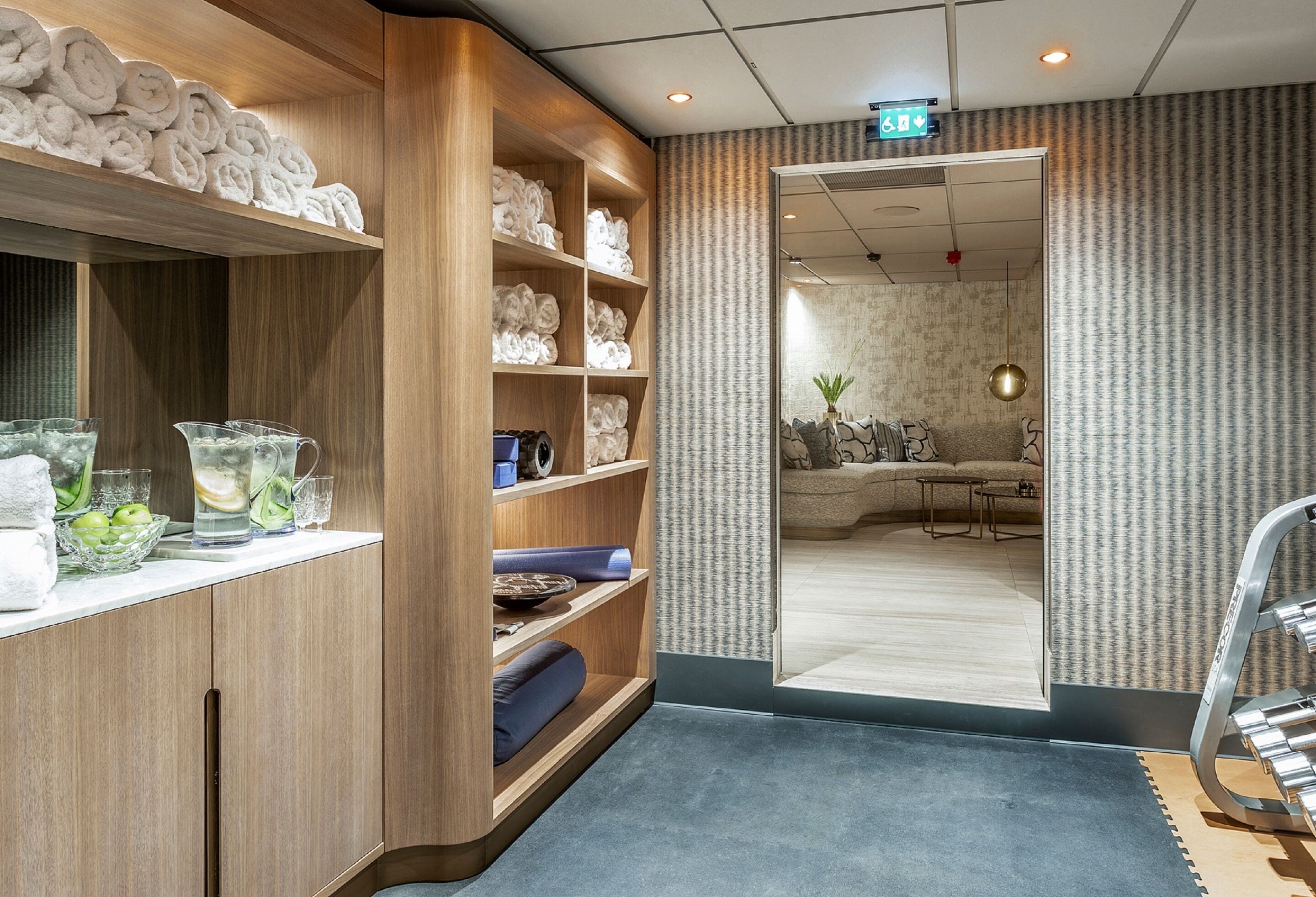 Et hotel lobby med træhylder, der viser håndklæder og toiletartikler, et siddeområde med sofa og bord, samt en væg med et mønster.
