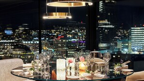 A dining table set with glasses, plates, and a candle, overlooking a cityscape at night. - Hotel Riverton (Gothenburg)