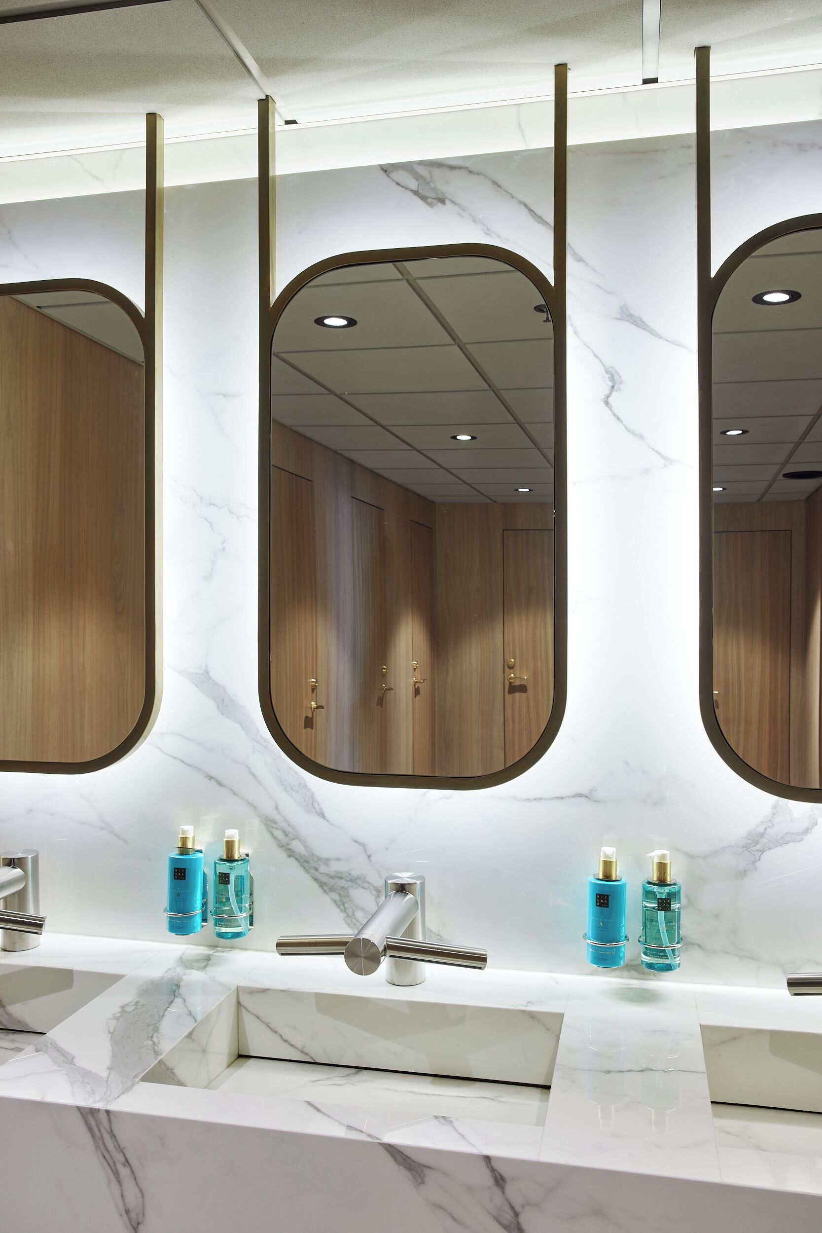 Une salle de bain avec un comptoir en marbre, trois miroirs et deux lavabos.