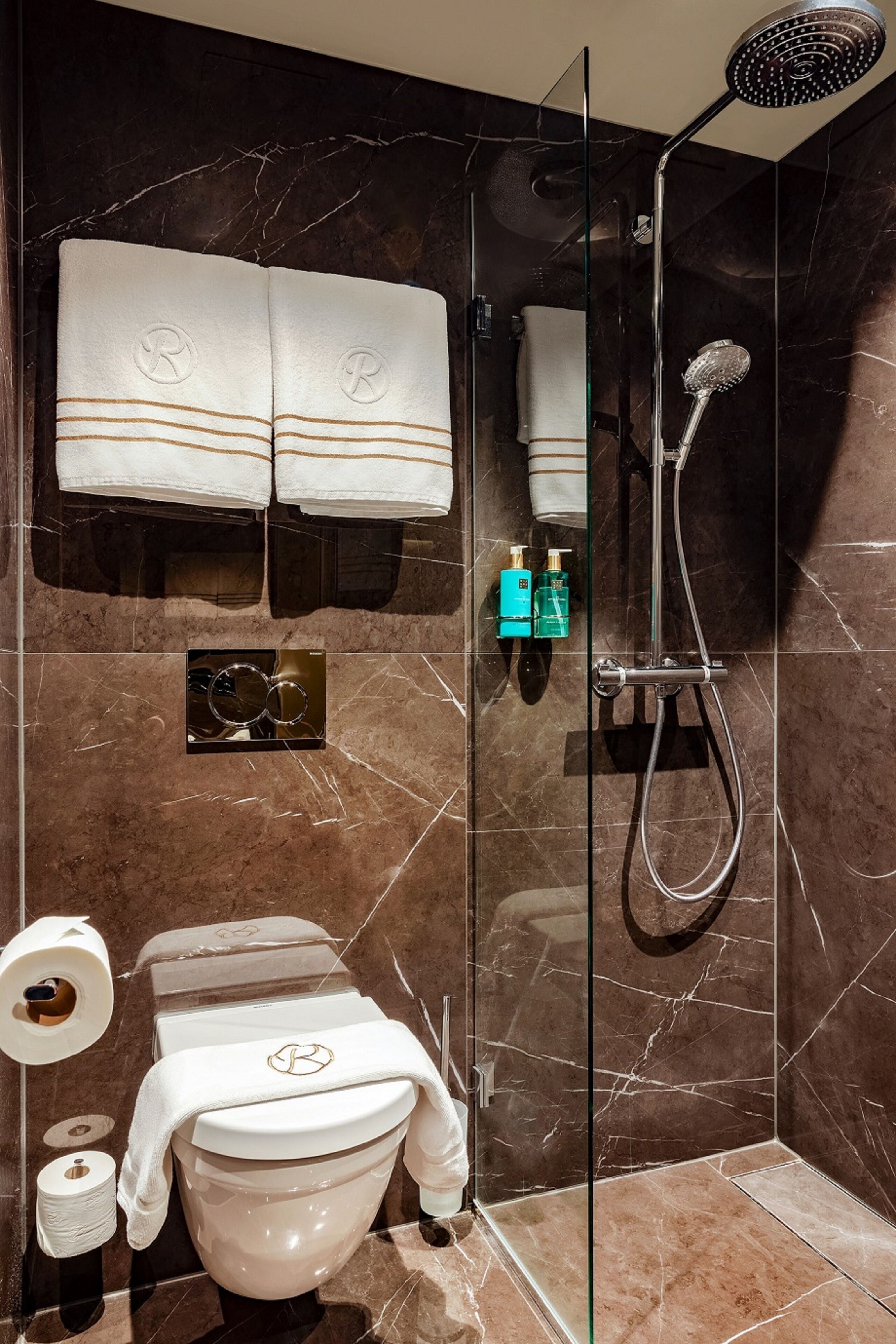 A modern bathroom with a glass-enclosed shower, a toilet with a towel, and a towel rack with towels.