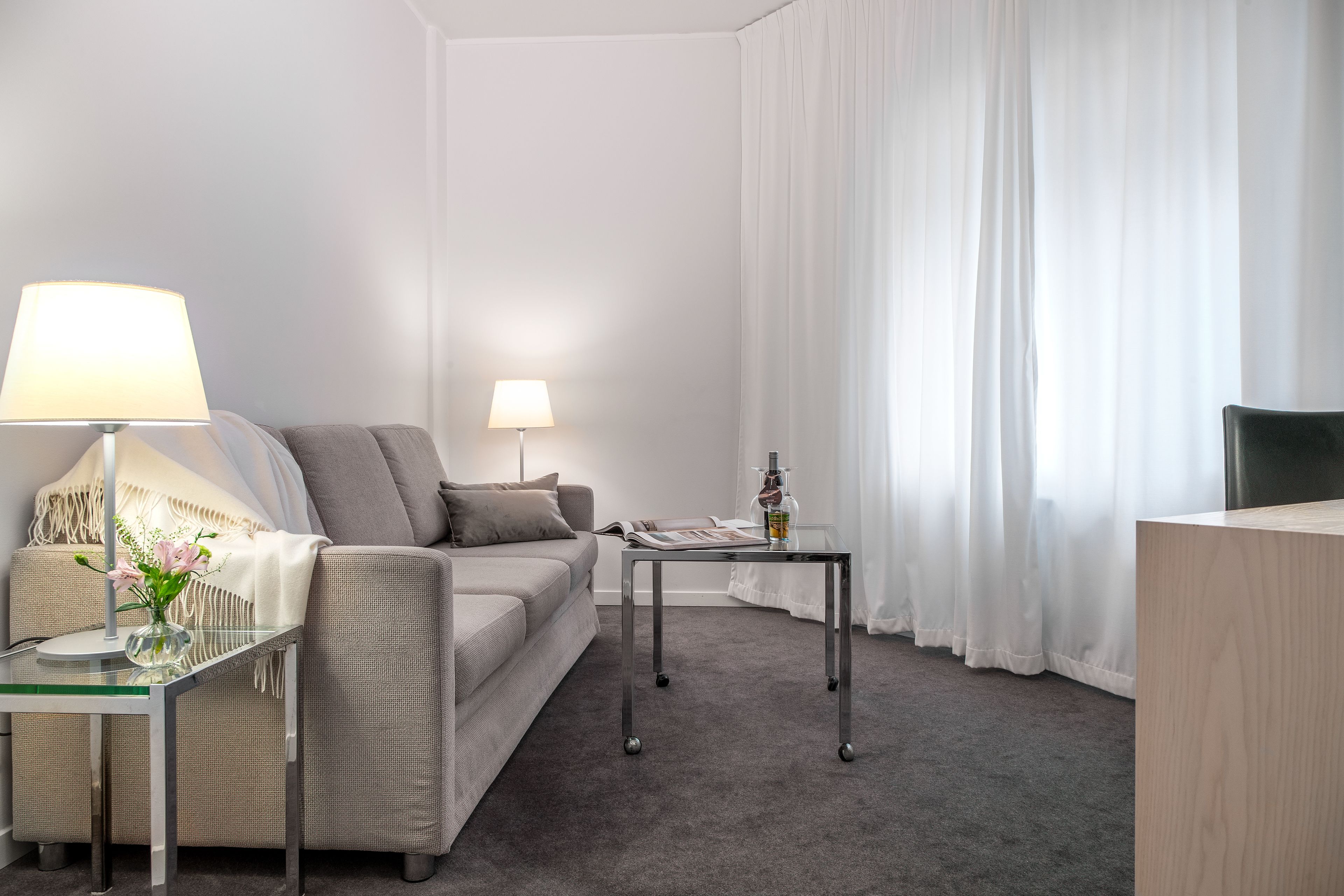 A modern living room with a sofa, two lamps, a glass table, and a magazine.