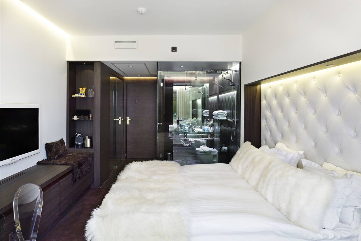 A modern hotel room with a large bed, a flat-screen TV, a vanity with a mirror, and a walk-in closet.