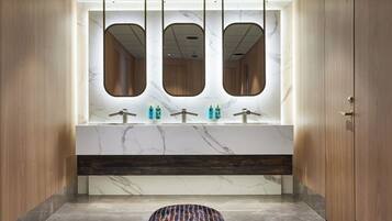 A modern bathroom with a marble vanity, three mirrors, and a patterned stool.