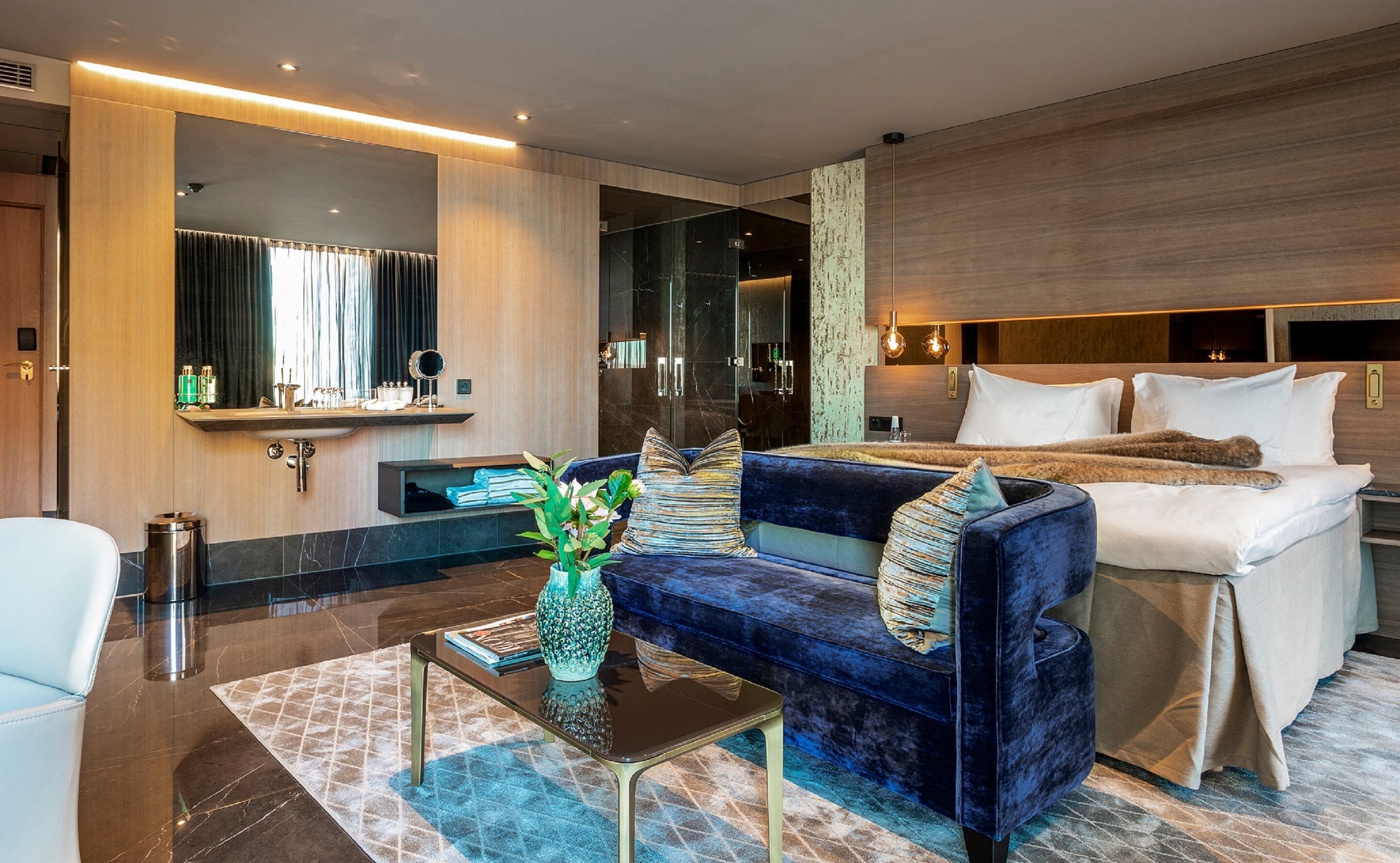 Une chambre d’hôtel moderne avec un grand lit, un canapé, une petite table avec un vase et un miroir.
