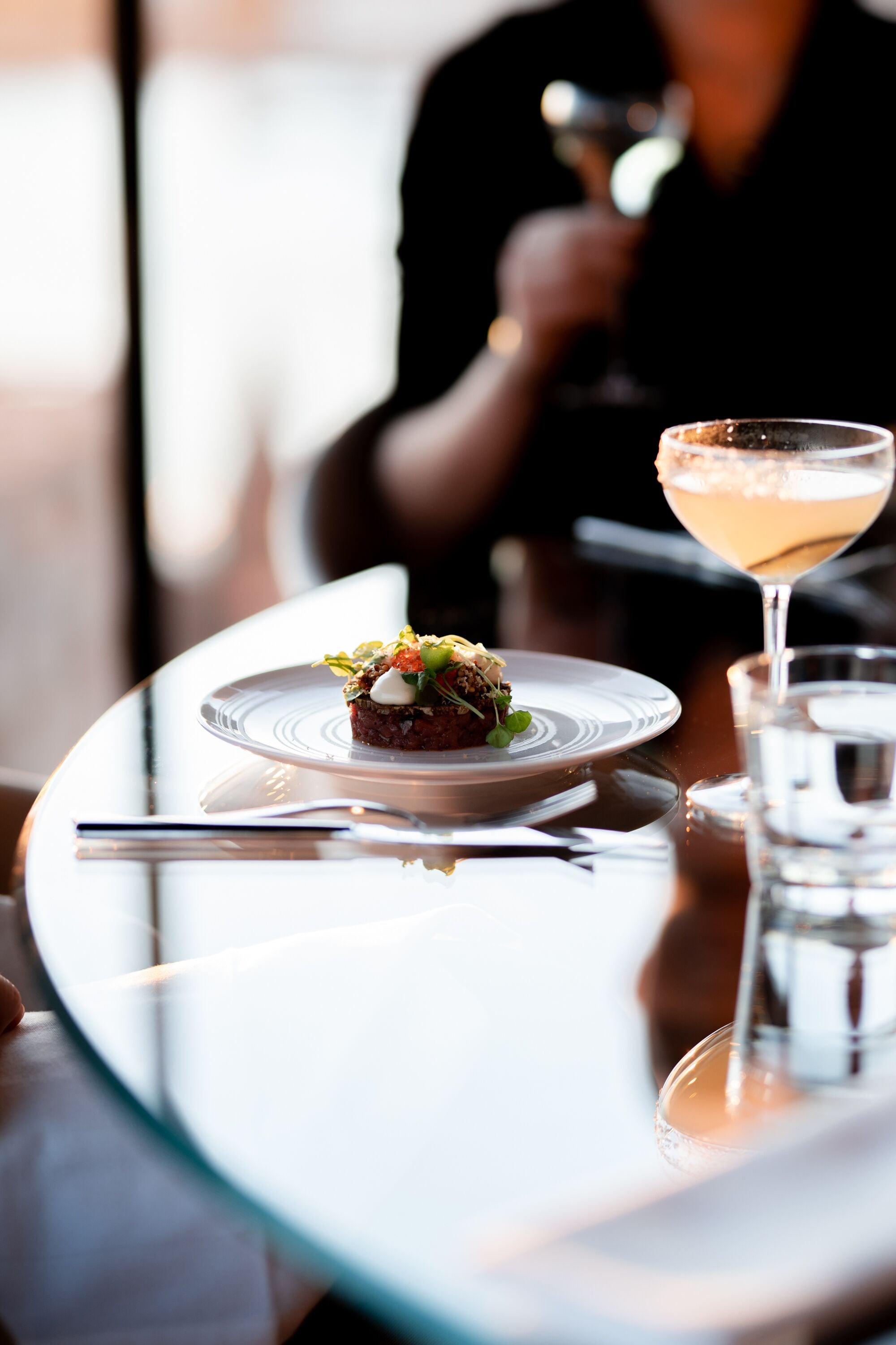 A dining table with a plate of food and a cocktail glass.