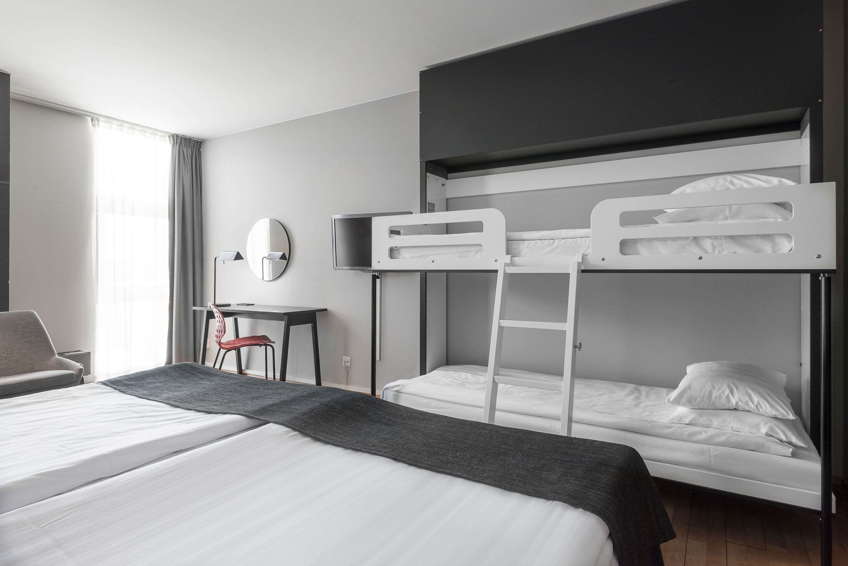 Een hotelkamer met twee bedden, een bureau, een stoel en een raam met gordijnen.