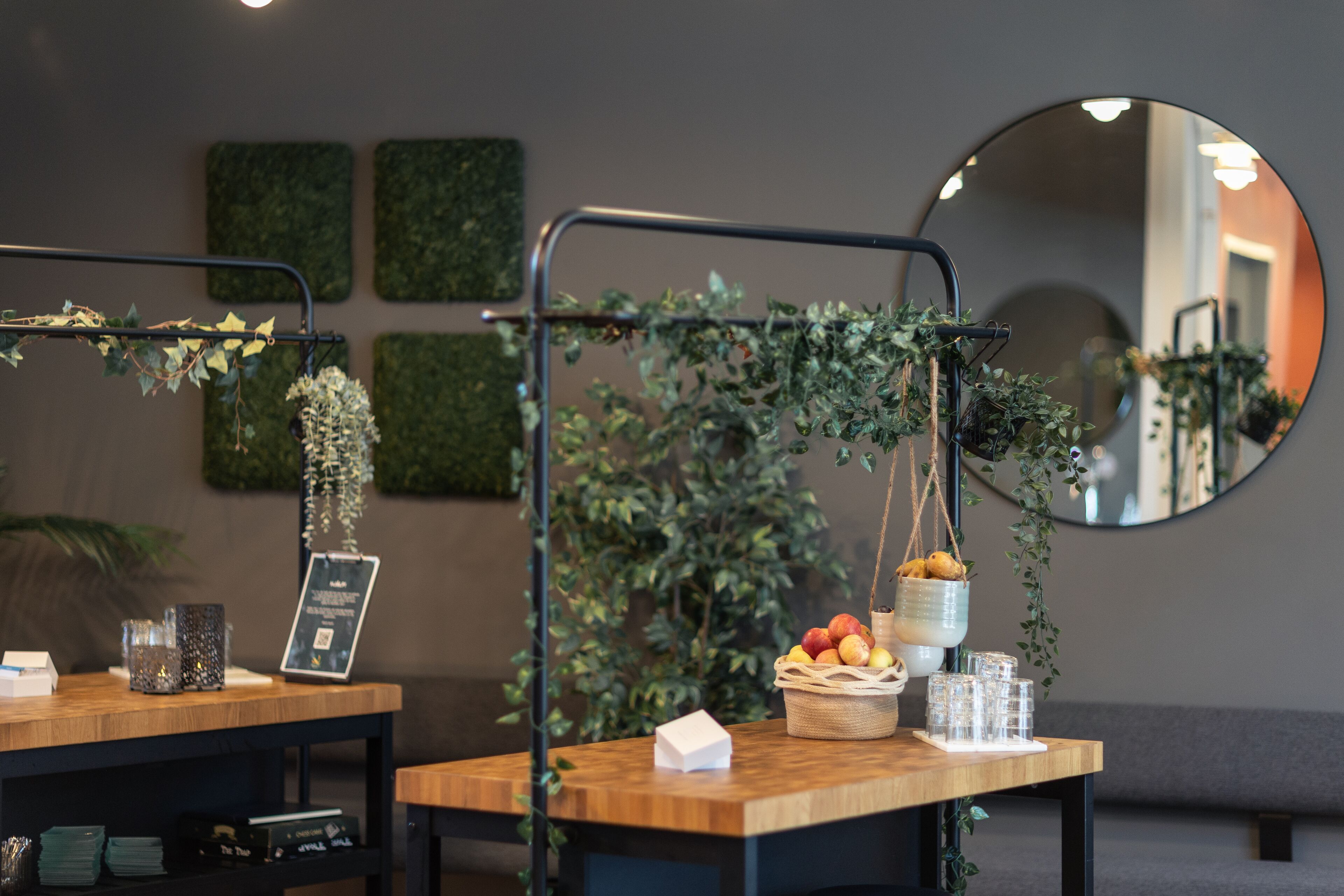 A reception area with a wooden desk, a hanging plant, a basket of fruit, and a mirror on the wall.