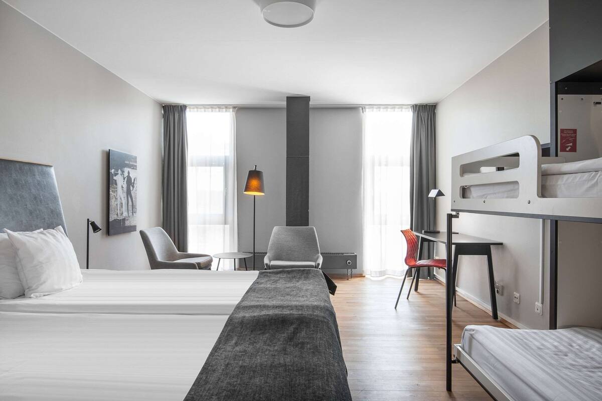 A modern hotel room with two beds, a desk, and a chair.