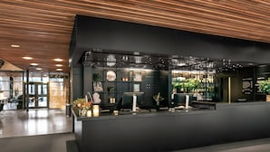 A modern reception area with a dark counter, a clock, and a bar area with plants. - Quality Hotel 11 (Gothenburg)