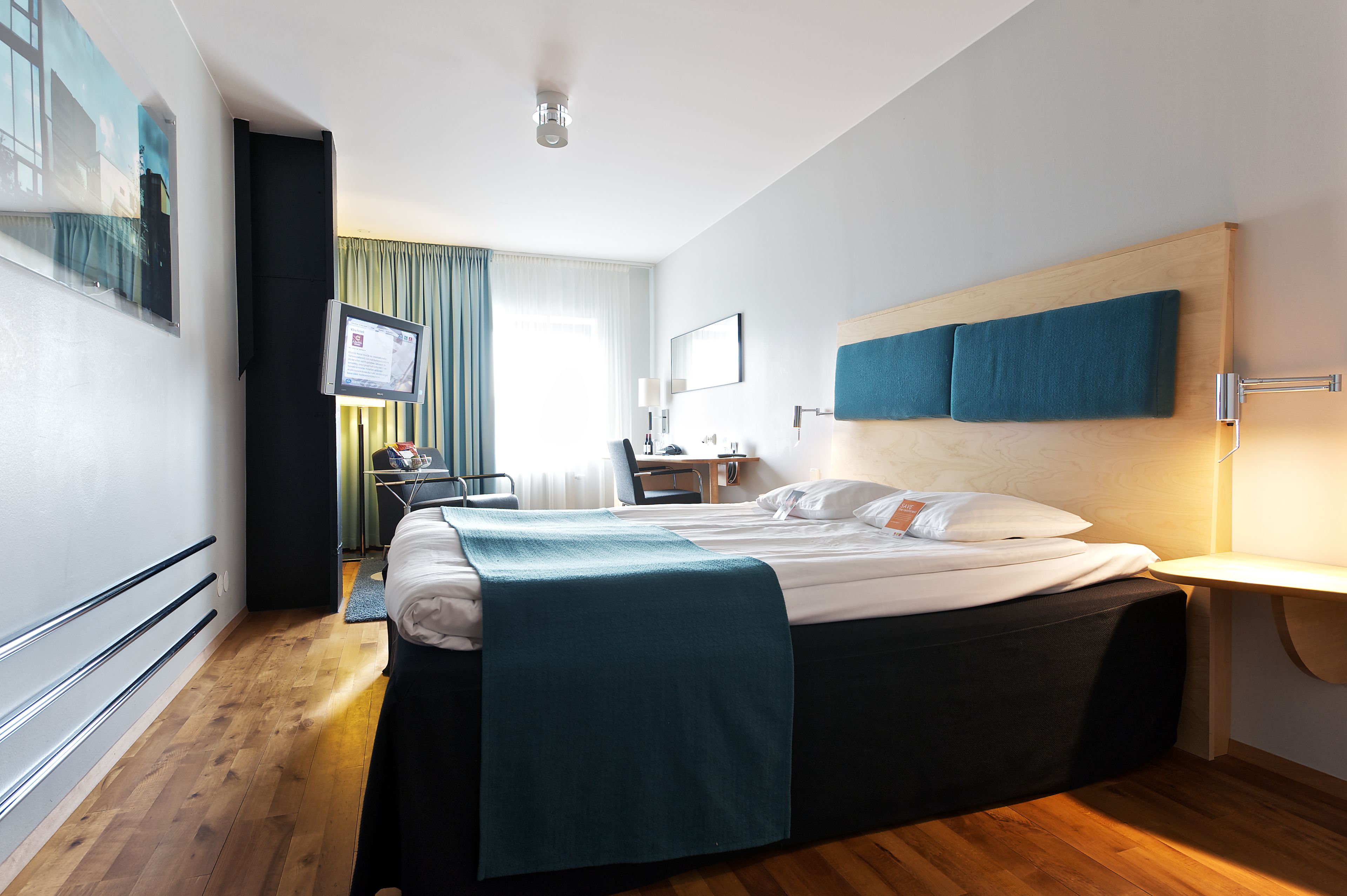 Hotelkamer met een bed, bureau, stoel, televisie en raam met gordijnen.