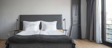 A modern bedroom with a large bed, two bedside tables, and a view of the outside through a window with curtains.