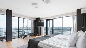 A modern hotel room with a large bed, a TV mounted on the wall, and a view of the city through large windows. - Quality Hotel 11 (Gothenburg)