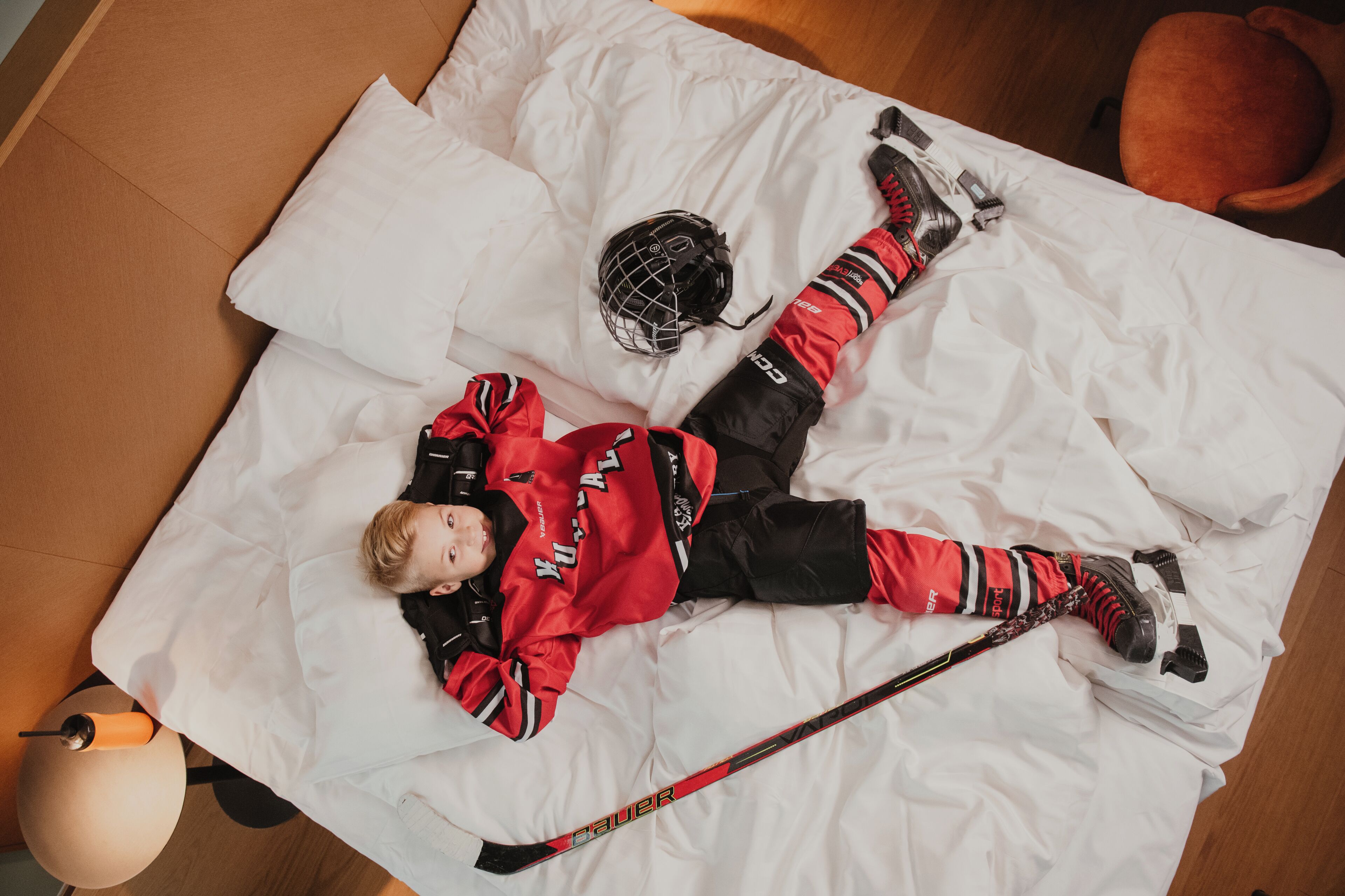 A person lying on a bed with a hockey stick, helmet, and protective gear.