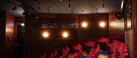 A theater with rows of red seats, wooden paneling, and stage lighting.