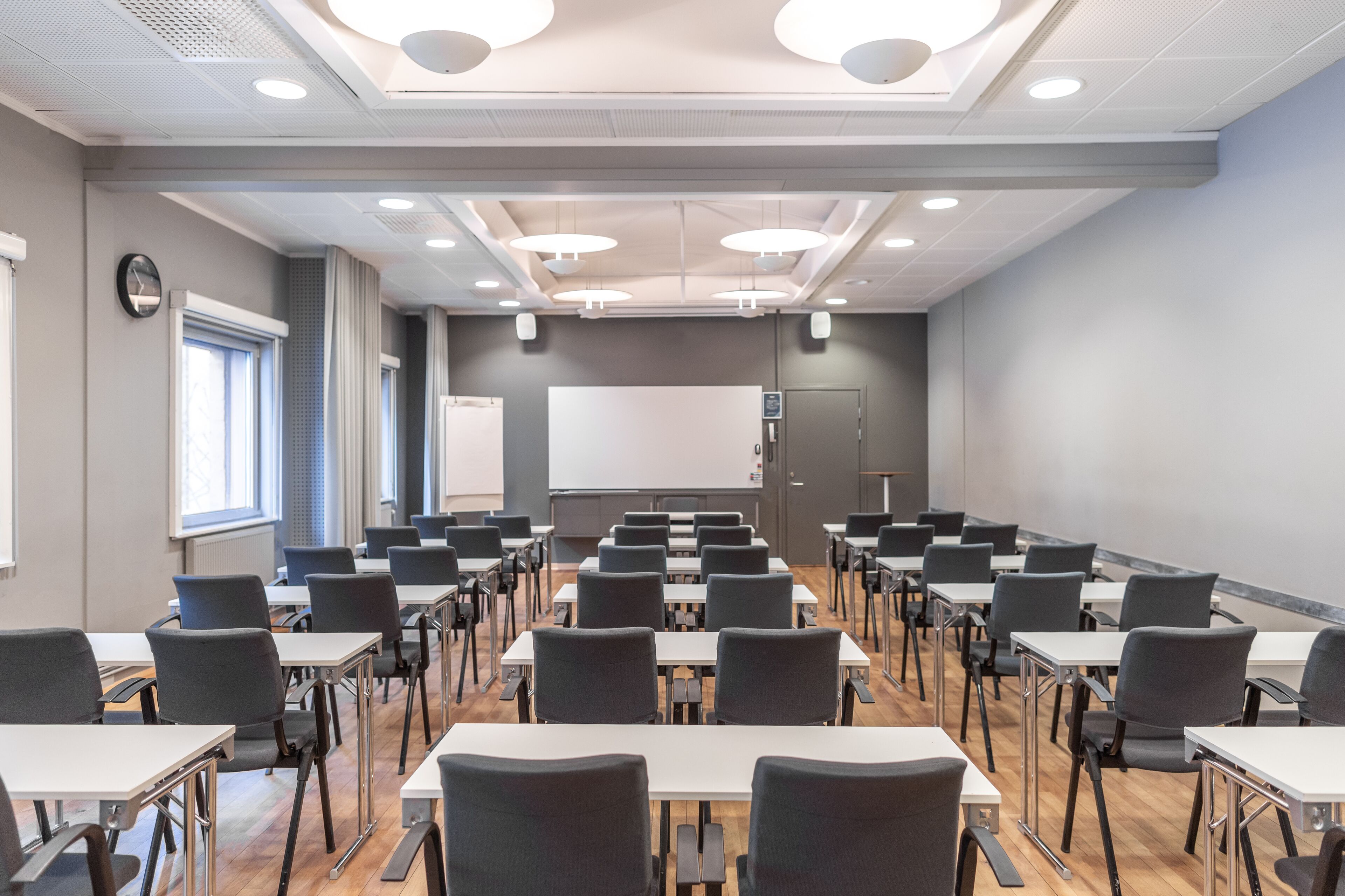 A conference room with rows of tables and chairs, a whiteboard, and a projector screen.