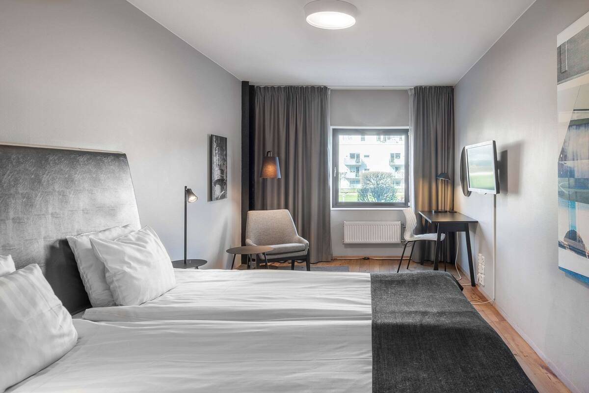 A modern hotel room with a large bed, a desk, a chair, and a TV.
