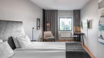 A modern hotel room with a large bed, a desk, a chair, and a TV.