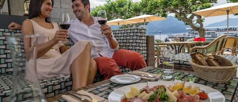 A couple seated at an outdoor table with a view of the sea, enjoying a meal and drinks.