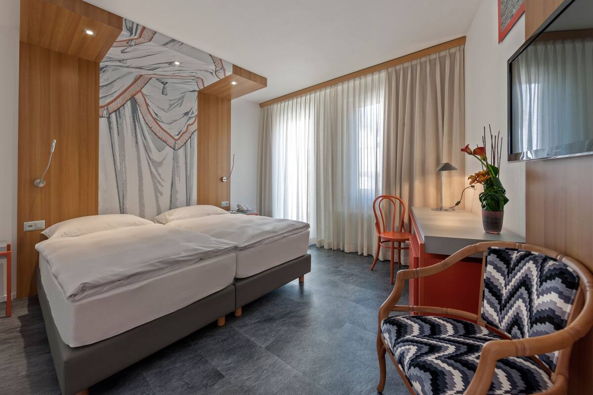 A modern hotel room with a large bed, a desk, a chair, and a potted plant.