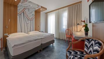 A modern hotel room with a large bed, a desk, a chair, and a potted plant.