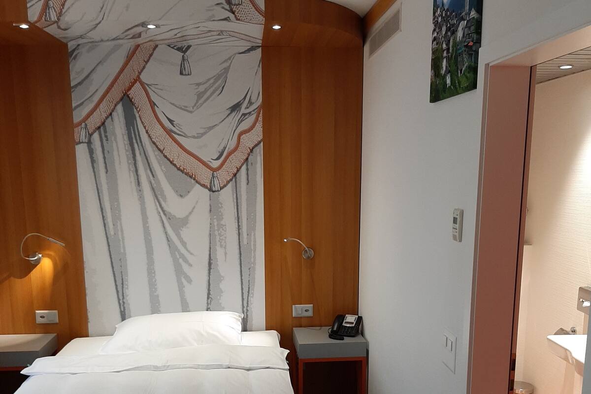 A hotel room with a bed, bedside tables, a telephone, and a bathroom visible through an open door.