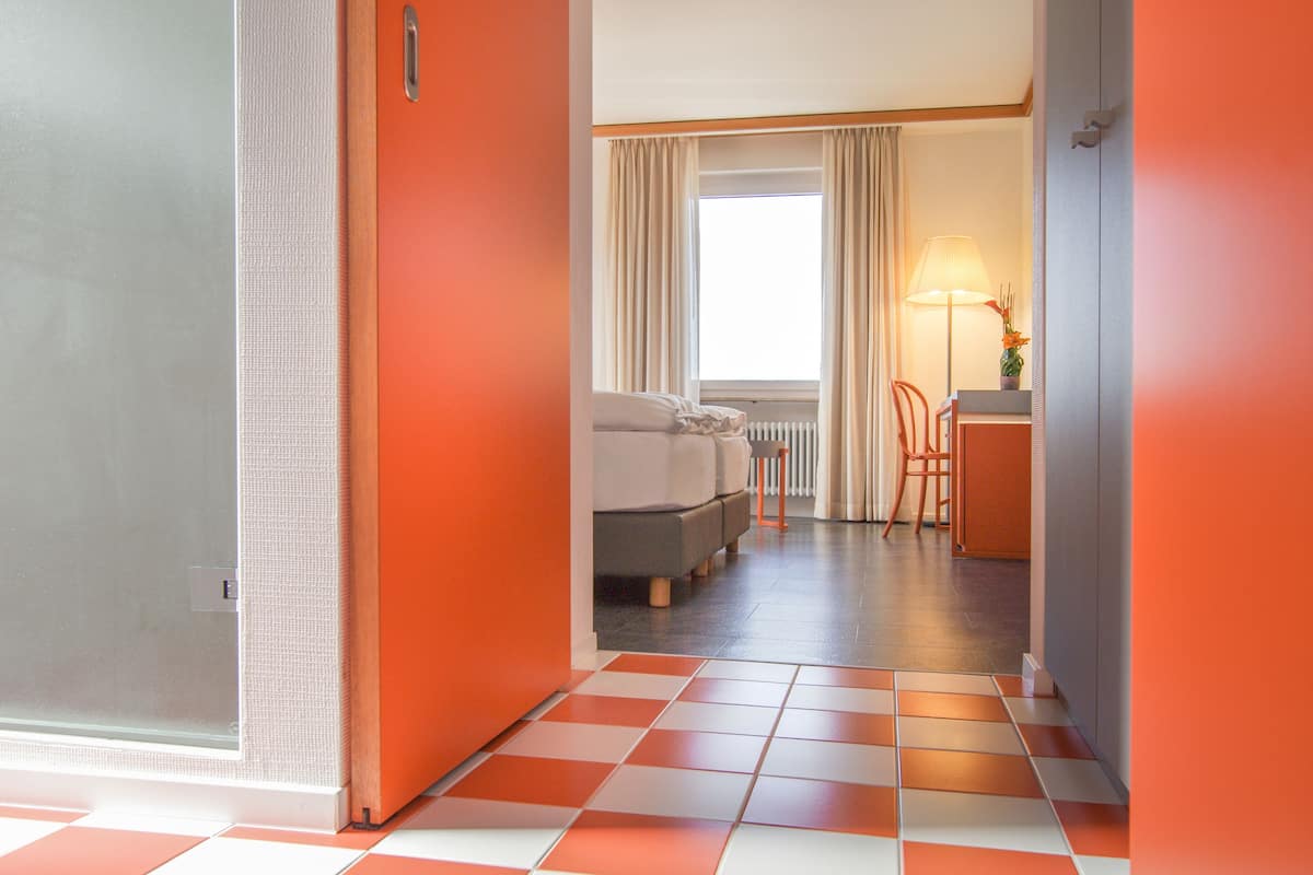 A hotel room with a checkered floor, a bed, a desk, and a window with curtains.