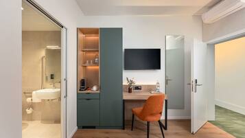 A modern bathroom with a shower, toilet, and sink. There is a wooden cabinet with a television above it and a chair in the room.