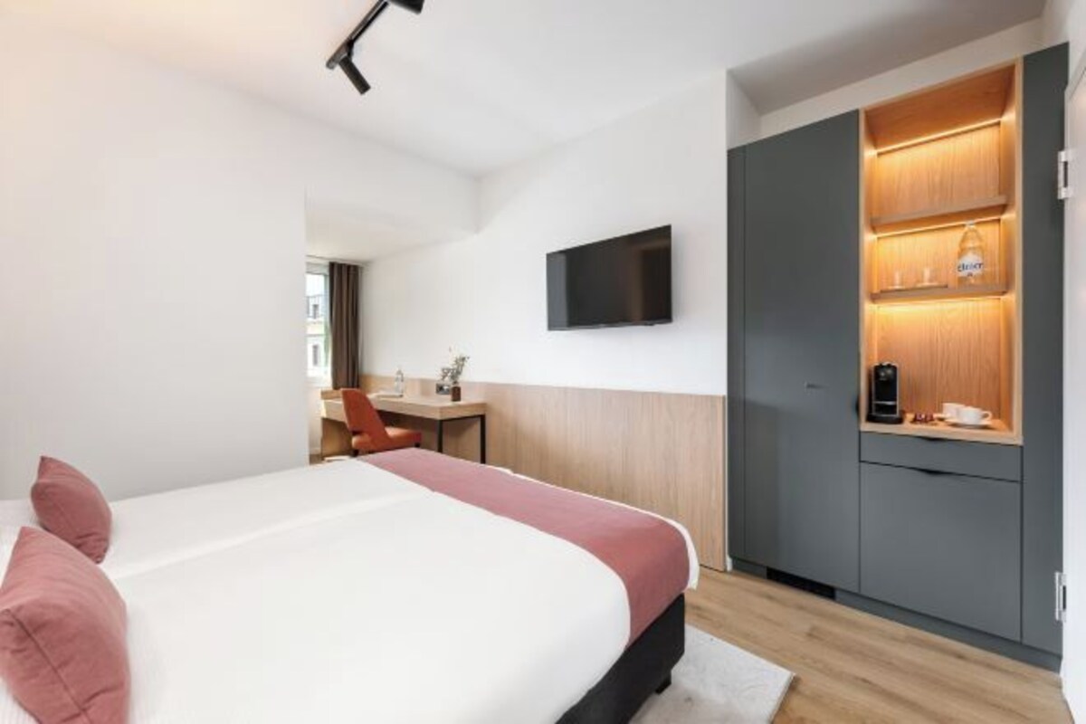 A hotel room with a bed, a desk, a TV, and a kitchenette.