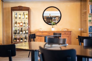 Zona pranzo con tavolo in legno, sedie nere, frigorifero per vino, uno specchio e una libreria.