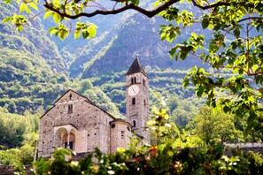 A historic stone building with a clock tower, surrounded by lush greenery and mountains. - Tailormade Hotel AL GIARDINETTO Biasca (Biasca)