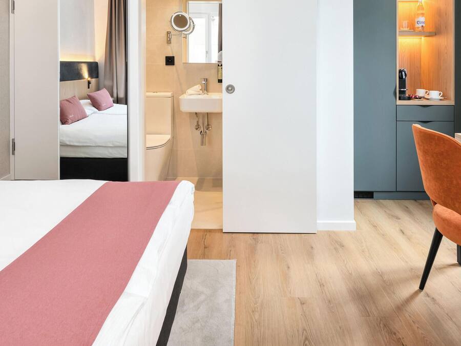 Habitación de hotel con cama, escritorio, silla, baño y vista a zonas verdes.