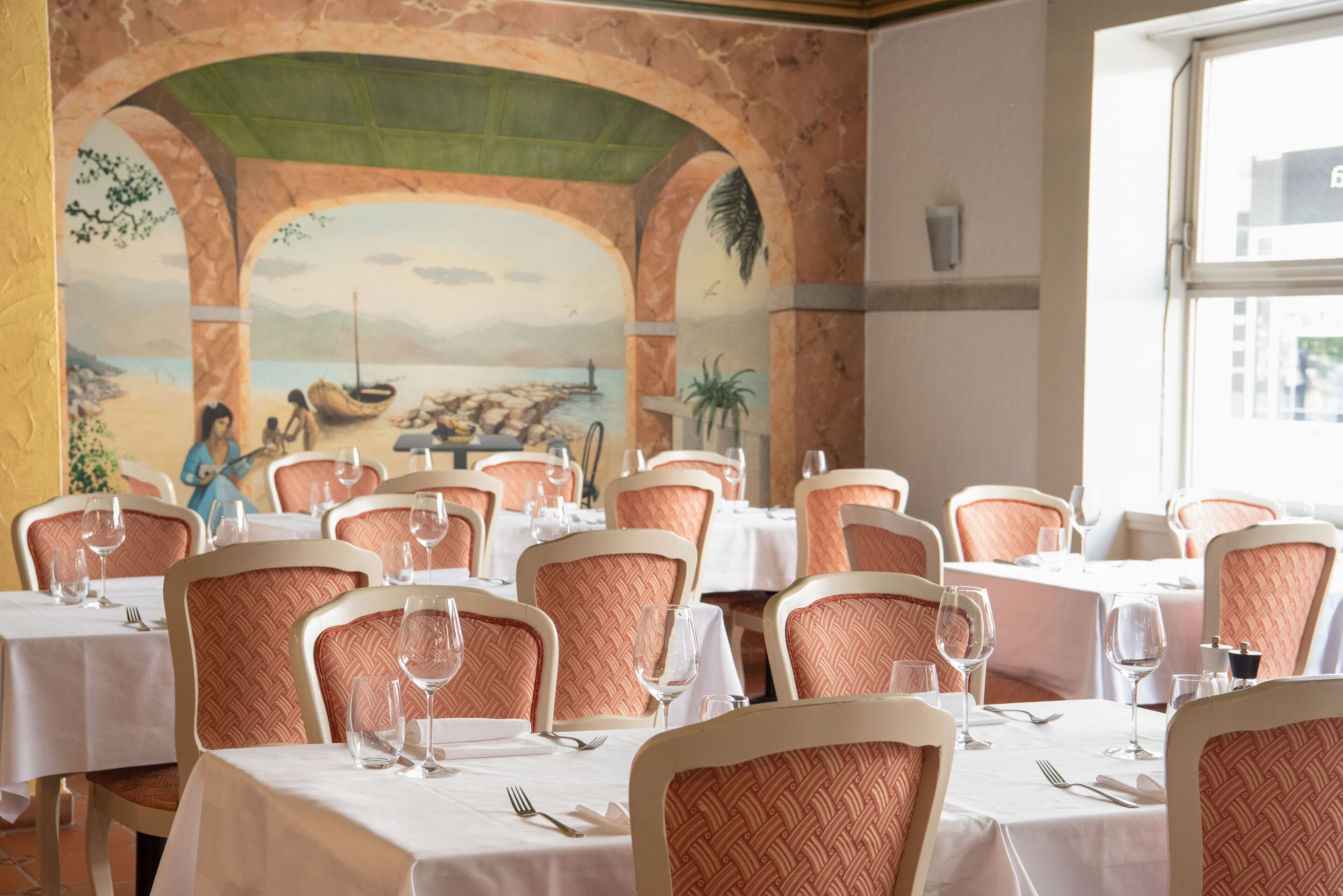 A restaurant with tables set for dining, featuring a mural of a beach scene on the wall.