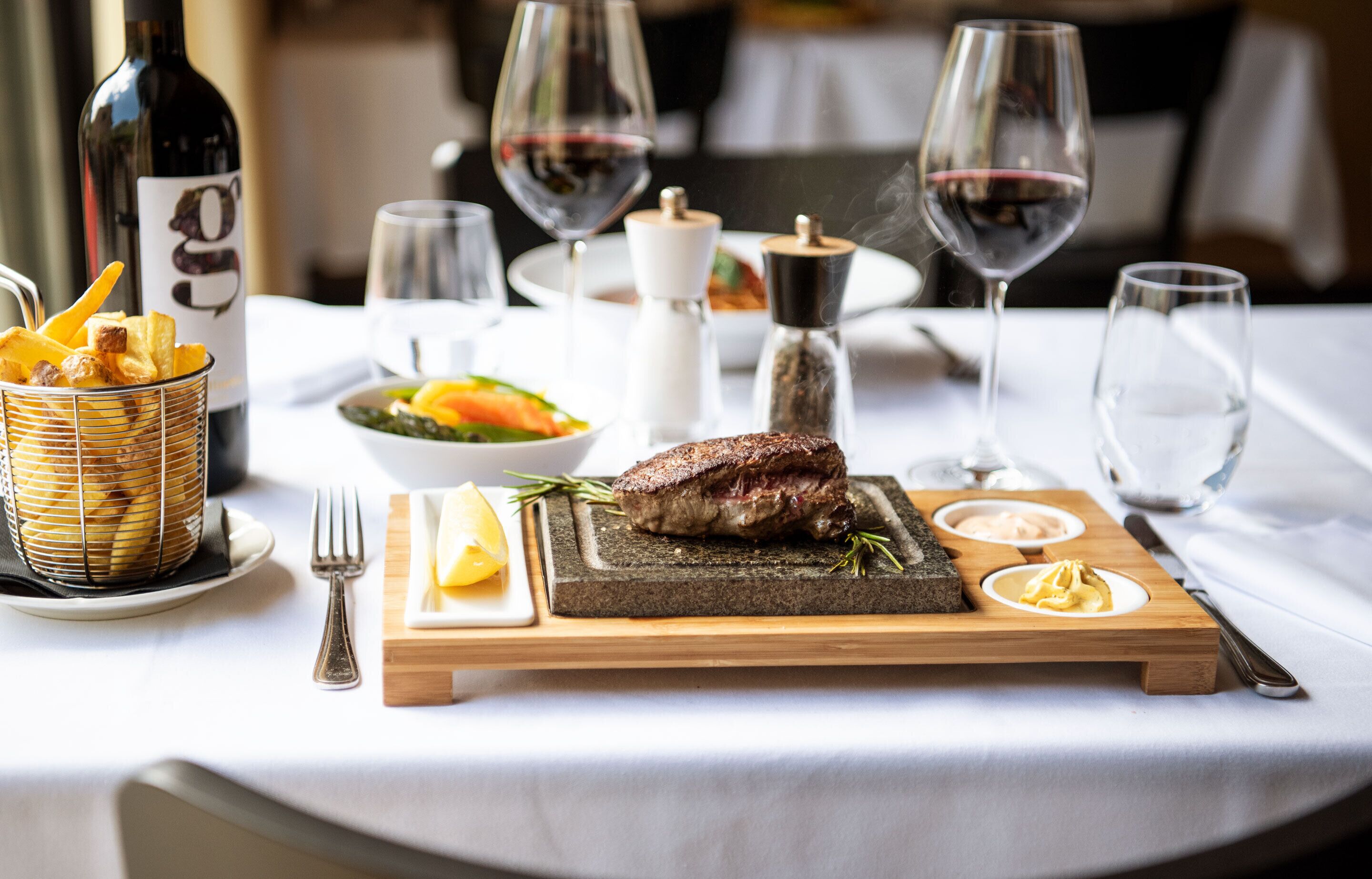 A dining table with a steak, salad, and bread basket.
