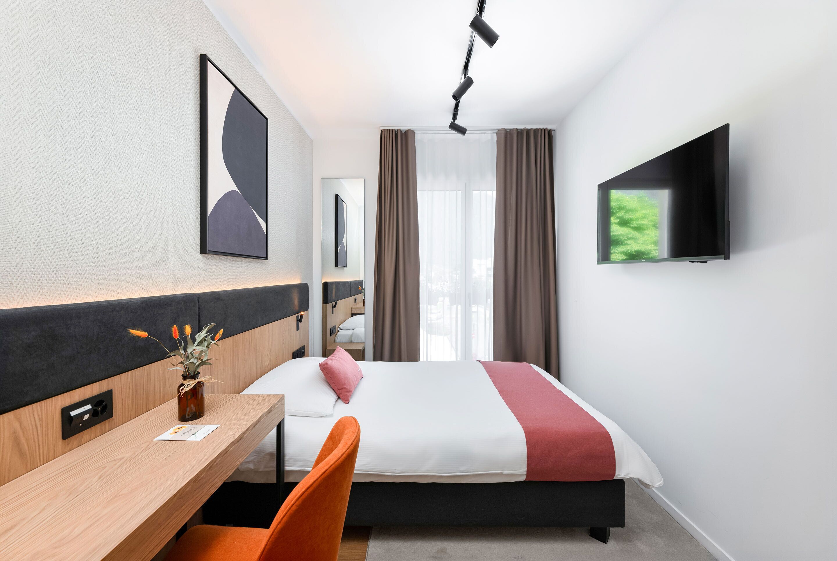 Habitación de hotel con cama, escritorio, silla, televisión y ventana con cortinas.