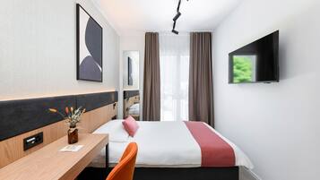 A hotel room with a bed, a desk, a chair, a TV, and a window with curtains.
