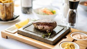A steak on a stone board with condiments and a salad in the background.