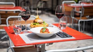 A dining table with a red tablecloth, a plate of spaghetti, two glasses of red wine, and a burger. - Tailormade Hotel AL GIARDINETTO Biasca (Biasca)