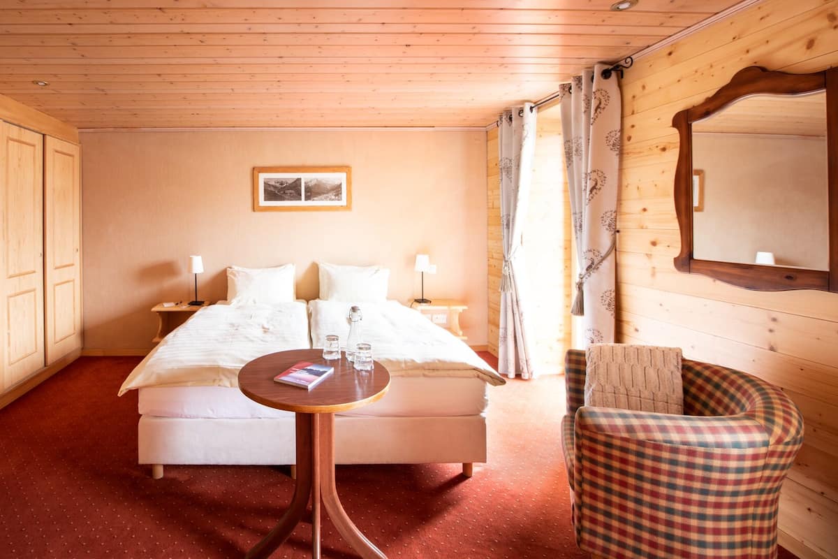 A cozy bedroom with a large bed, a small round table, a chair, and a wardrobe.