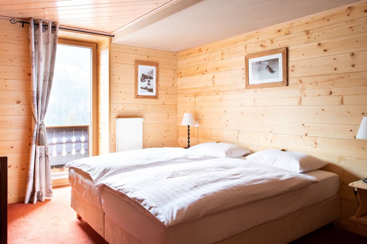 A wooden room with a bed, a chair, a table, and a window with curtains.